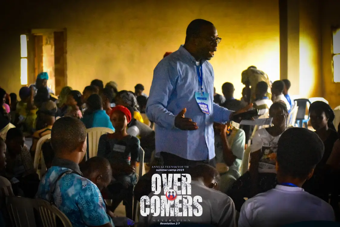 A man in a blue shirt speaks to a seated group of people in a dimly lit room. The event logo Out Corners is visible at the bottom center of the image.